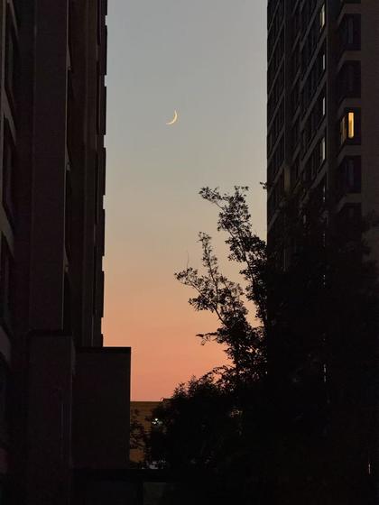 Crescent moon between dark buildings at dusk
